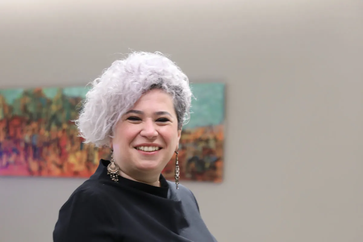 Didem Sökmen, renkli bir tablonun önünde gülümserken