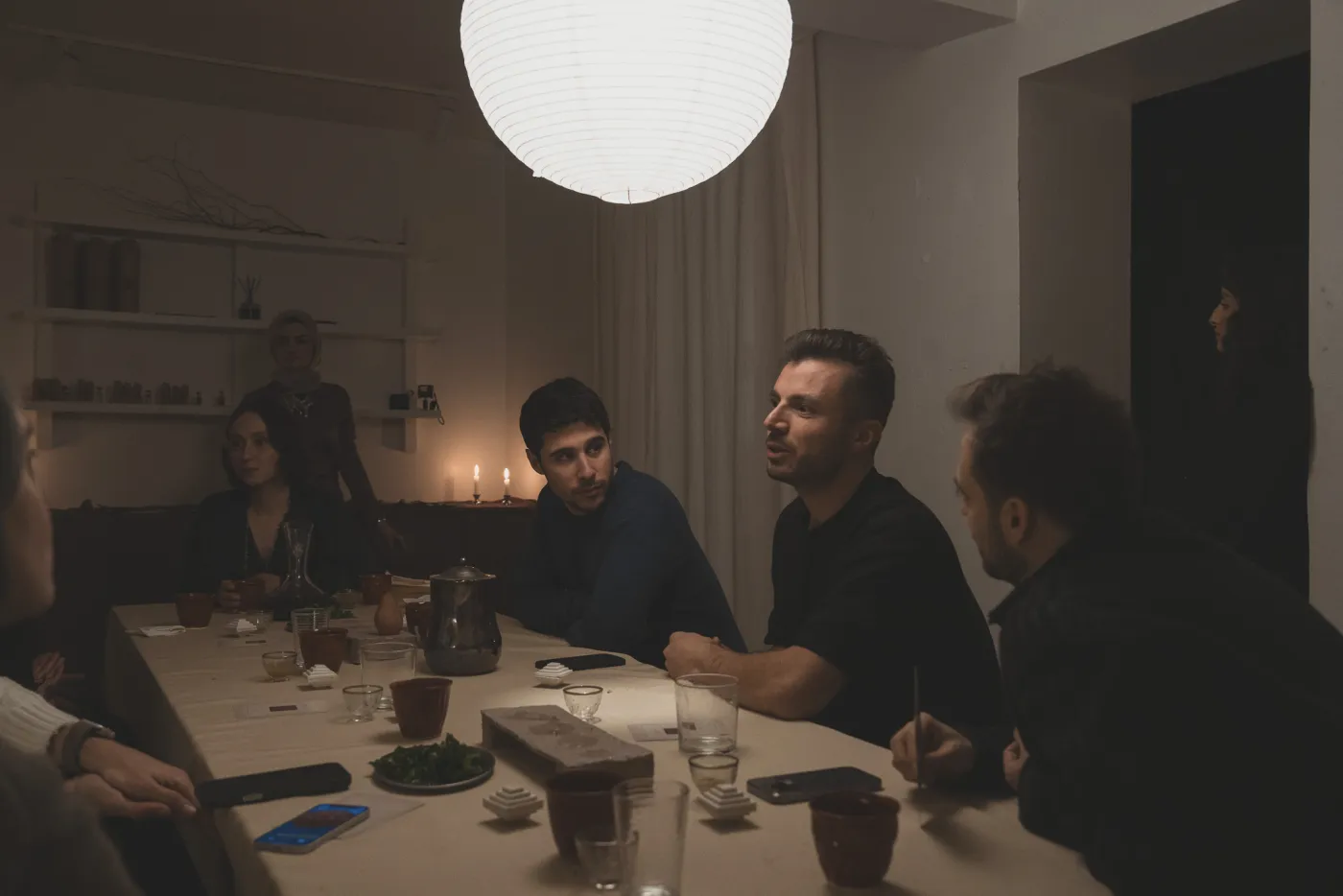 Uzun bir masada mum ışığında konuşan katılımcılar